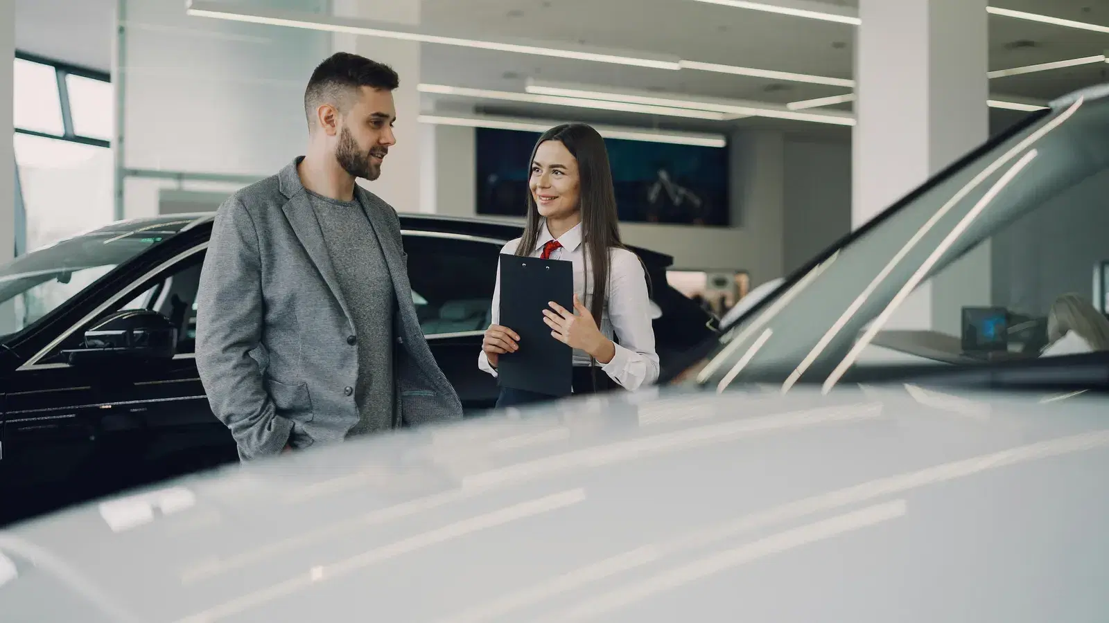 Man consults with salesperson in modern car dealership showroom.